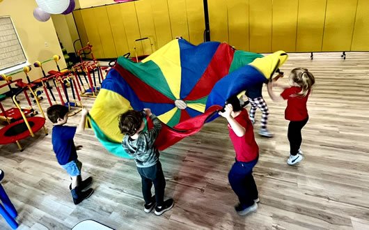 Parachute games support gross motor development, strengthen muscles, and encourage cooperative group play.